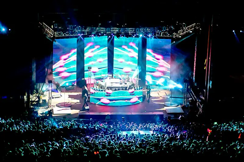 Wide shot of an arena concert stage and crowd under full production lighting