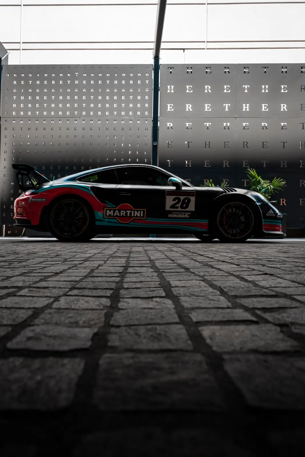 Porsche GT3 in Martini livery parked on cobblestone, shot low and moody