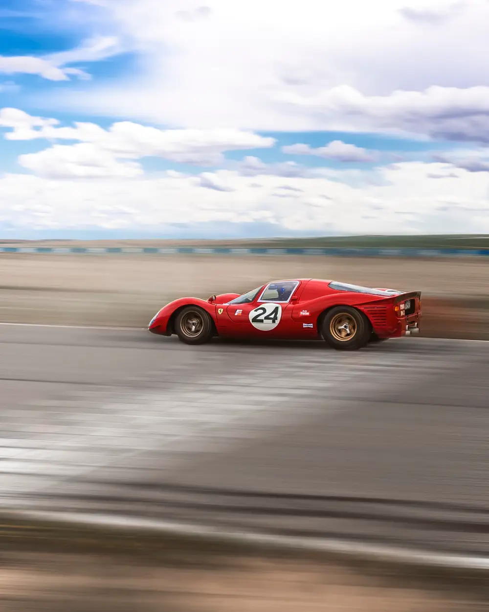 Red vintage endurance race car at speed crossing the finish line, panning shot