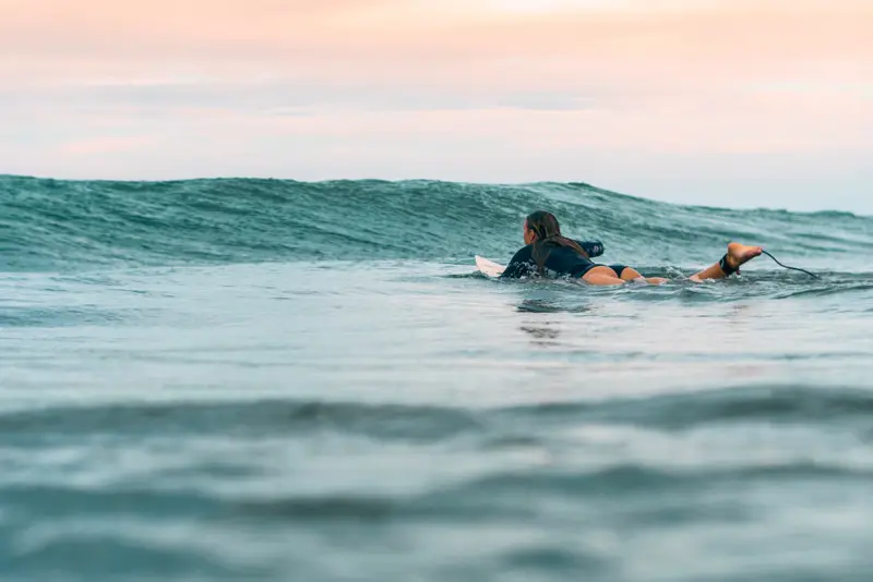 Surfer paddling over a rising wave at dawn, shot from the water