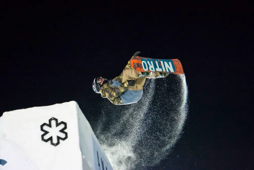Snowboarder throwing a rooster tail of snow off a ledge feature at night at the Winter X Games